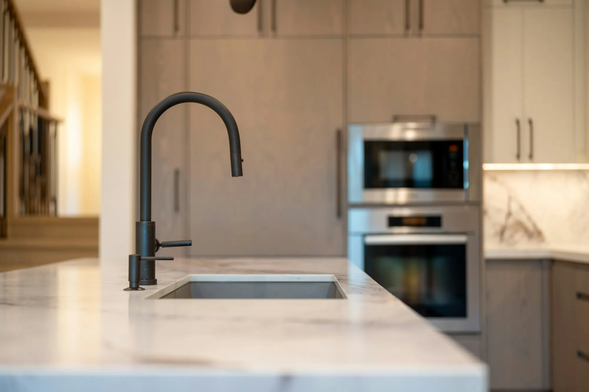 A matte-black faucet over a marble island sink in a bright modern kitchen