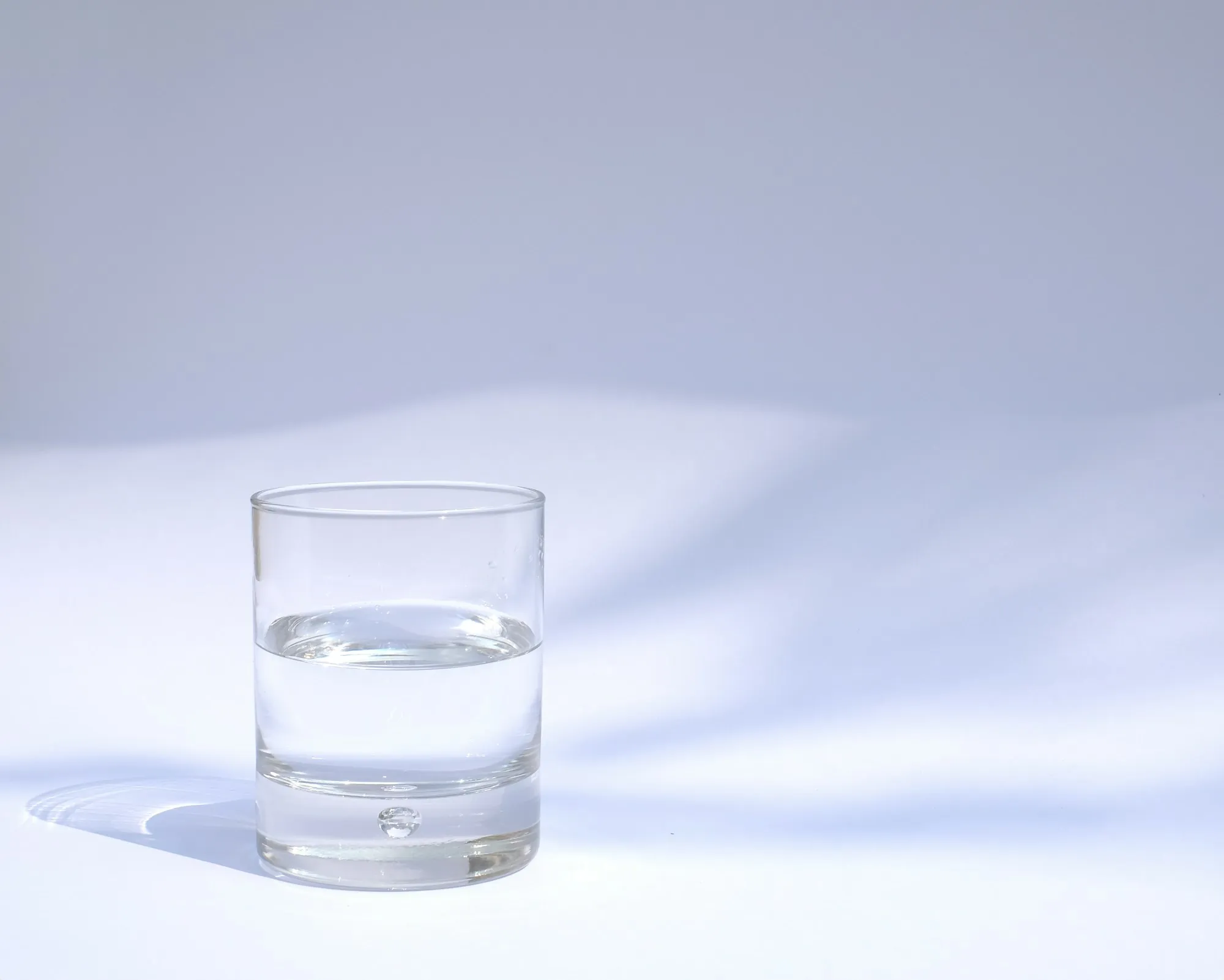 A single glass of water on a pale table