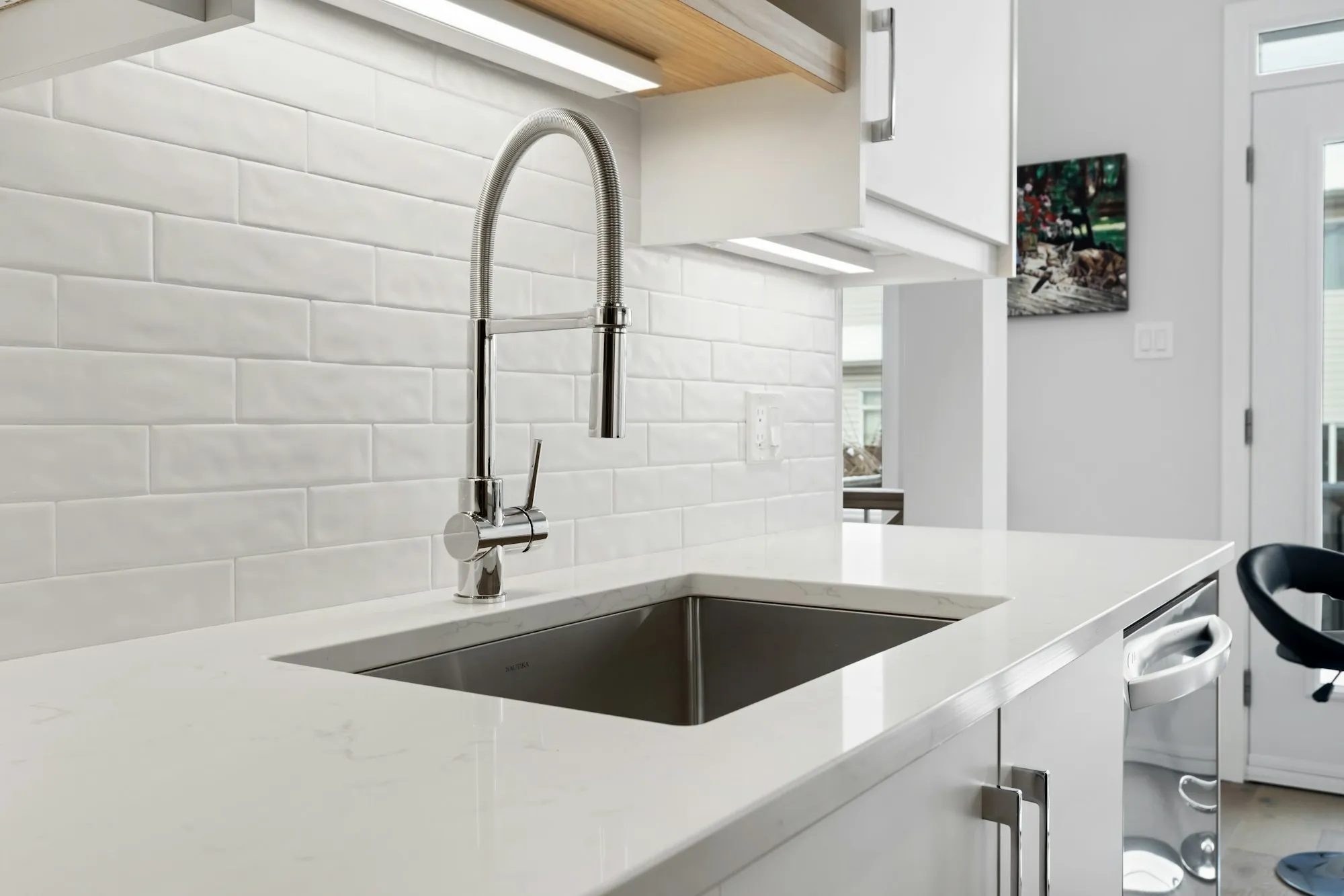 A white kitchen with a tall stainless faucet over an undermount sink