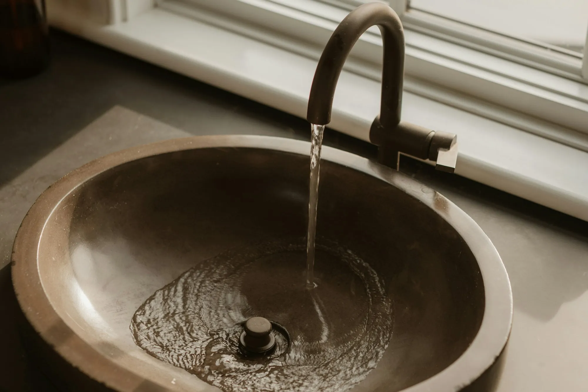 A copper-toned vessel sink with water running from a dark faucet