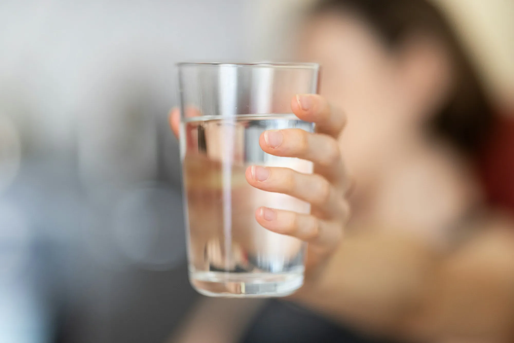 A hand holding a clear glass of drinking water