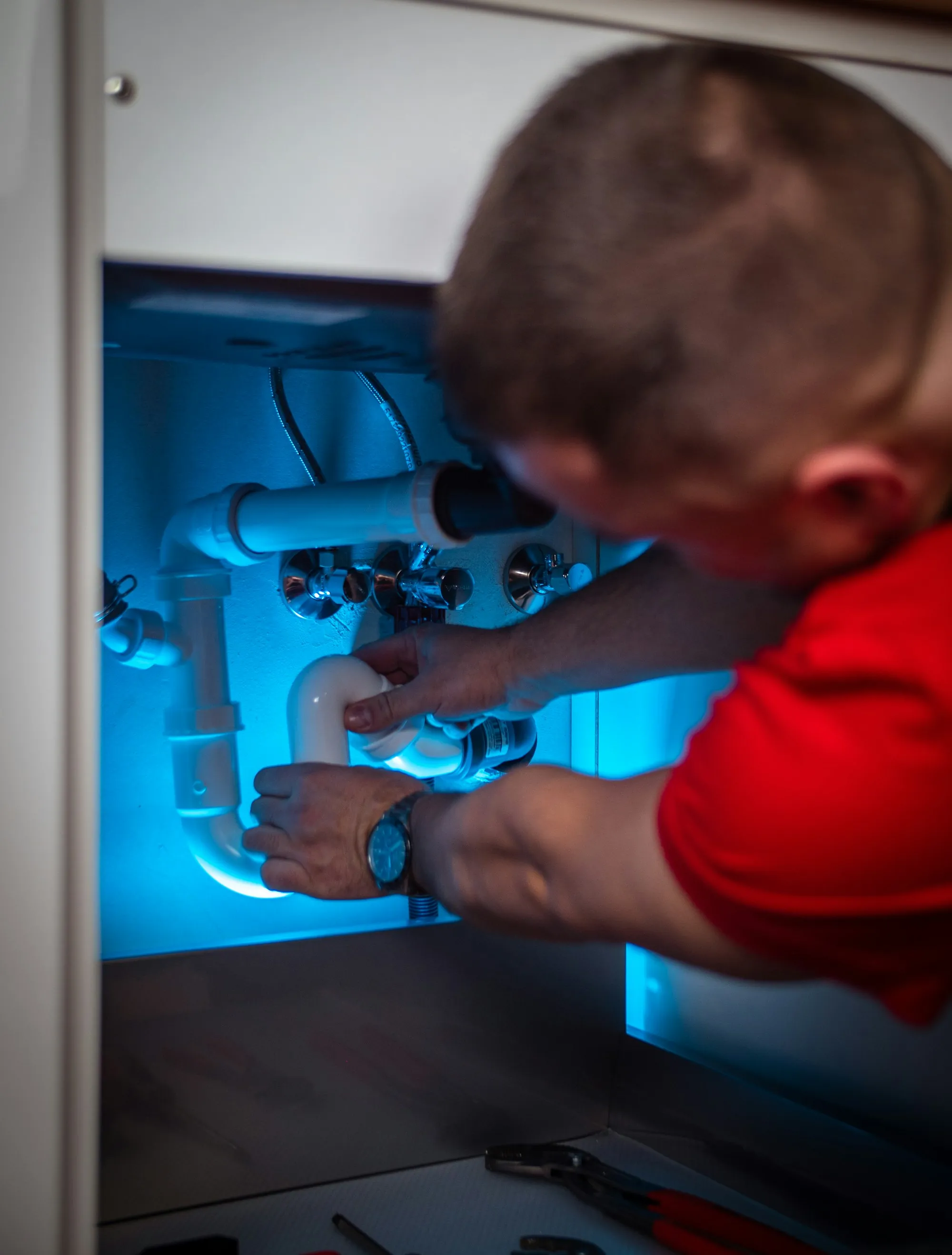 A technician working on plumbing under a kitchen sink