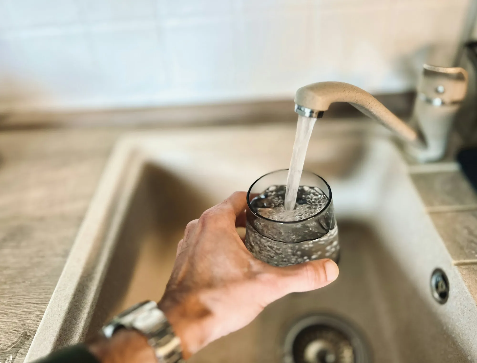 A hand filling a glass with water from a kitchen faucet