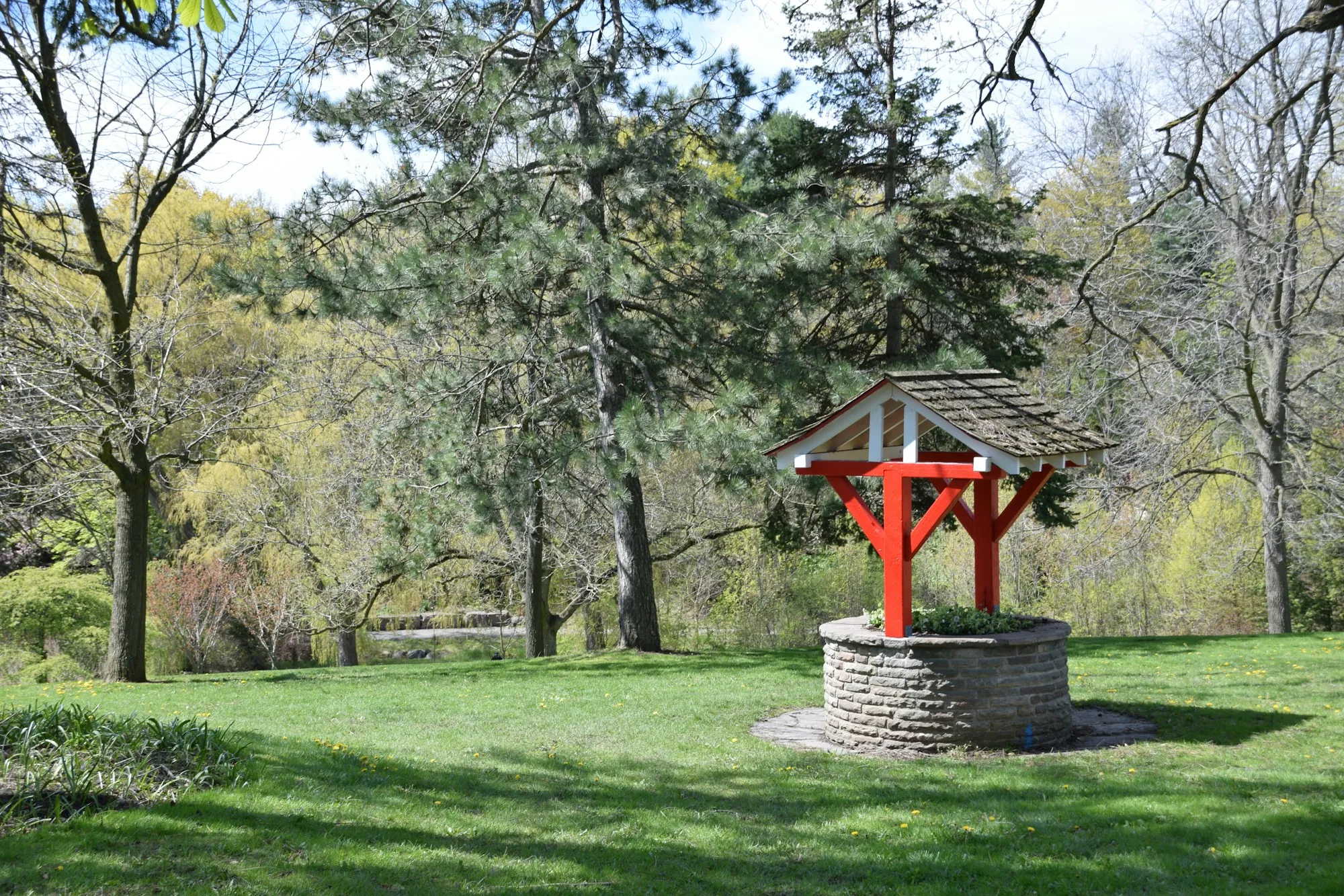 A traditional well with a small roof standing on a green lawn